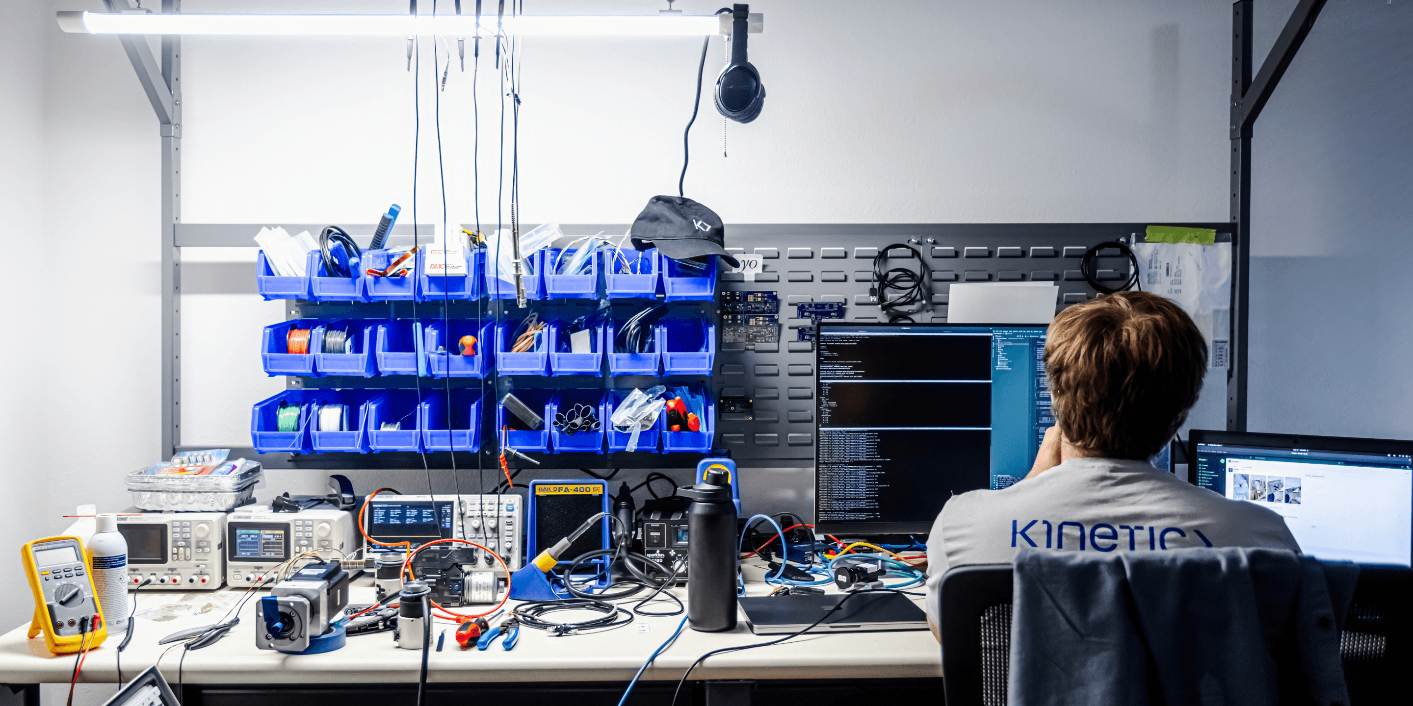 Kinetic CTO and Co-founder Sander Marques sits at a desk in the company’s headquarters. His back is turned to the camera. In the foreground is a wall filled with various electronic hardware components.