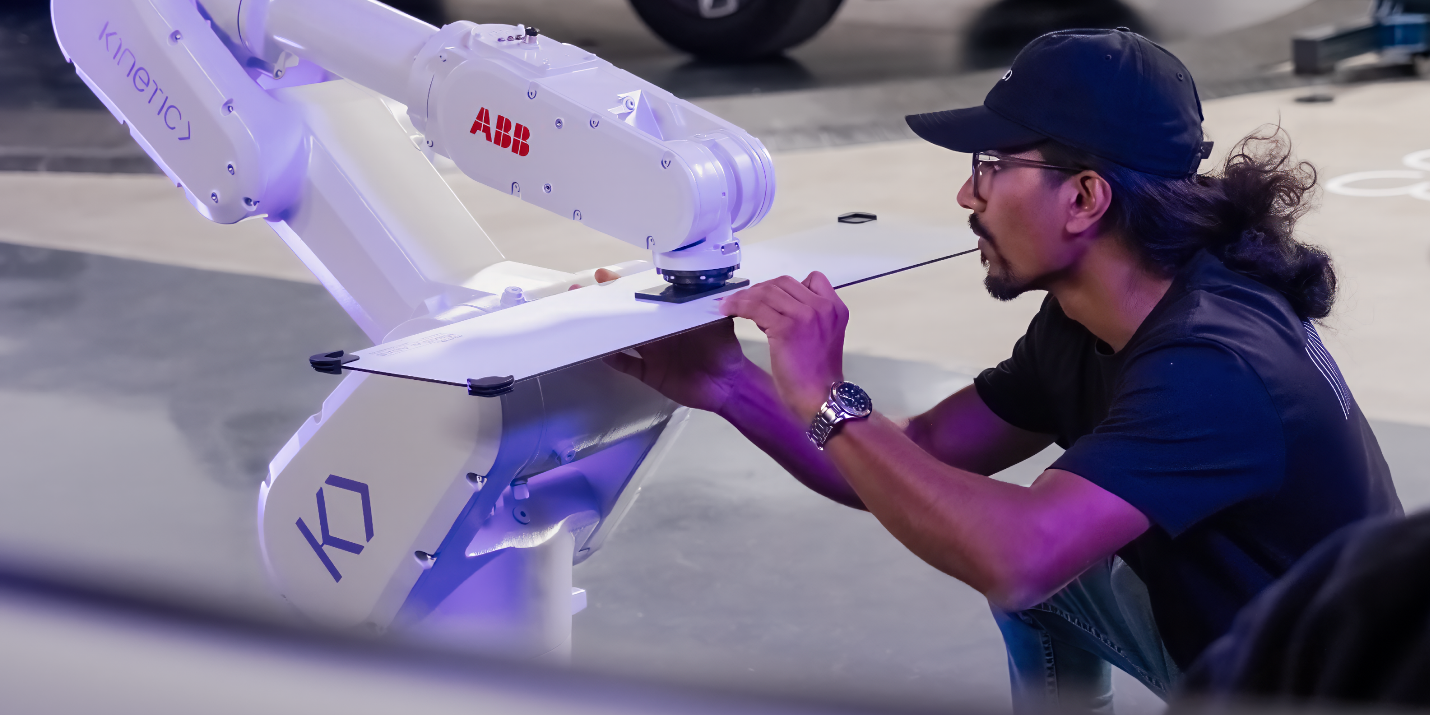 A Kinetic technician crouches down to inspect a robot arm, ensuring a secure connection between the arm and a calibration card.