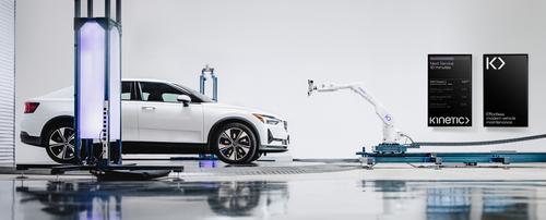 An image showing a Kinetic vehicle maintenance bay. A white Polestar car sits on a turntable, ready to be calibrated by a robotic arm. Two vertical digital screens display a list of cars currently in the service queue, along with the copy line “effortless modern vehicle maintenance.”